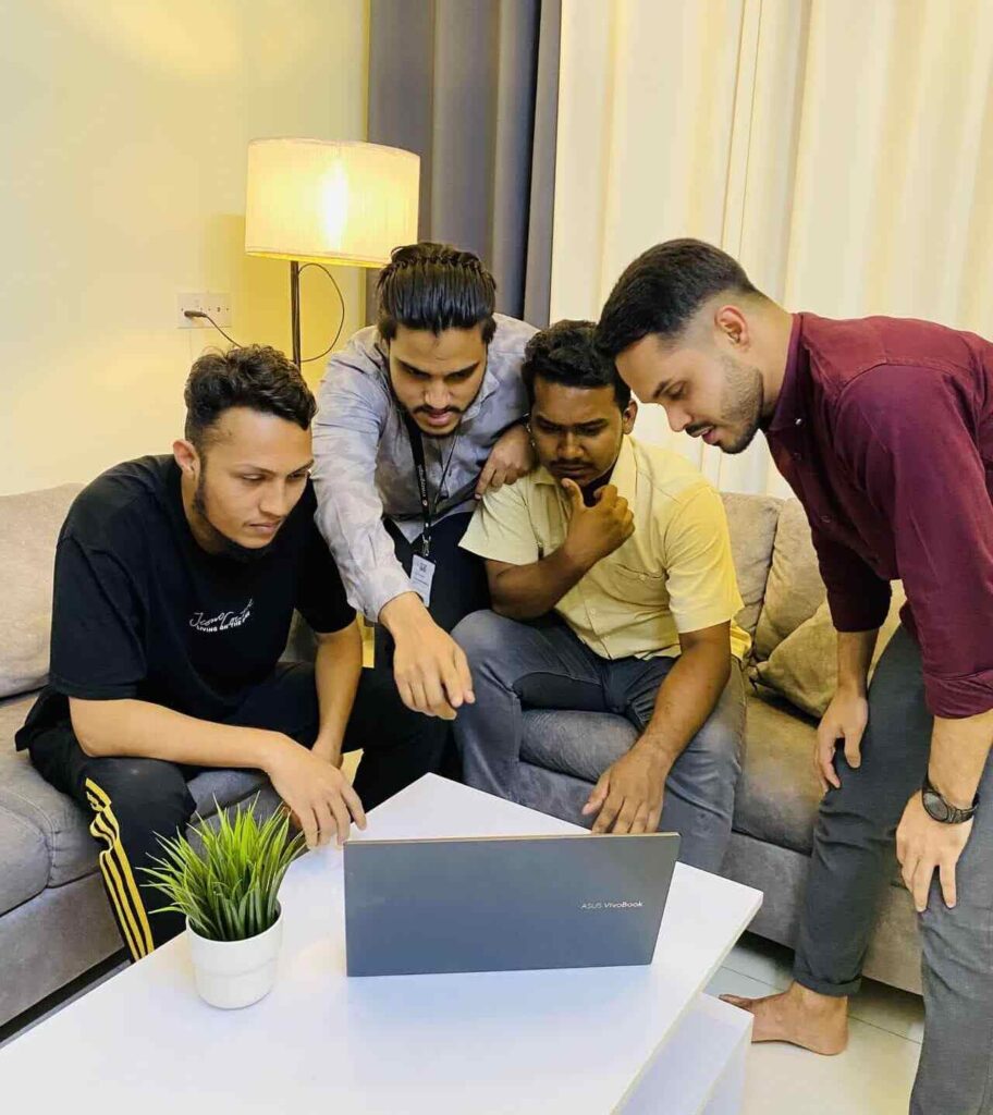 a group of four young men gathered around a laptop